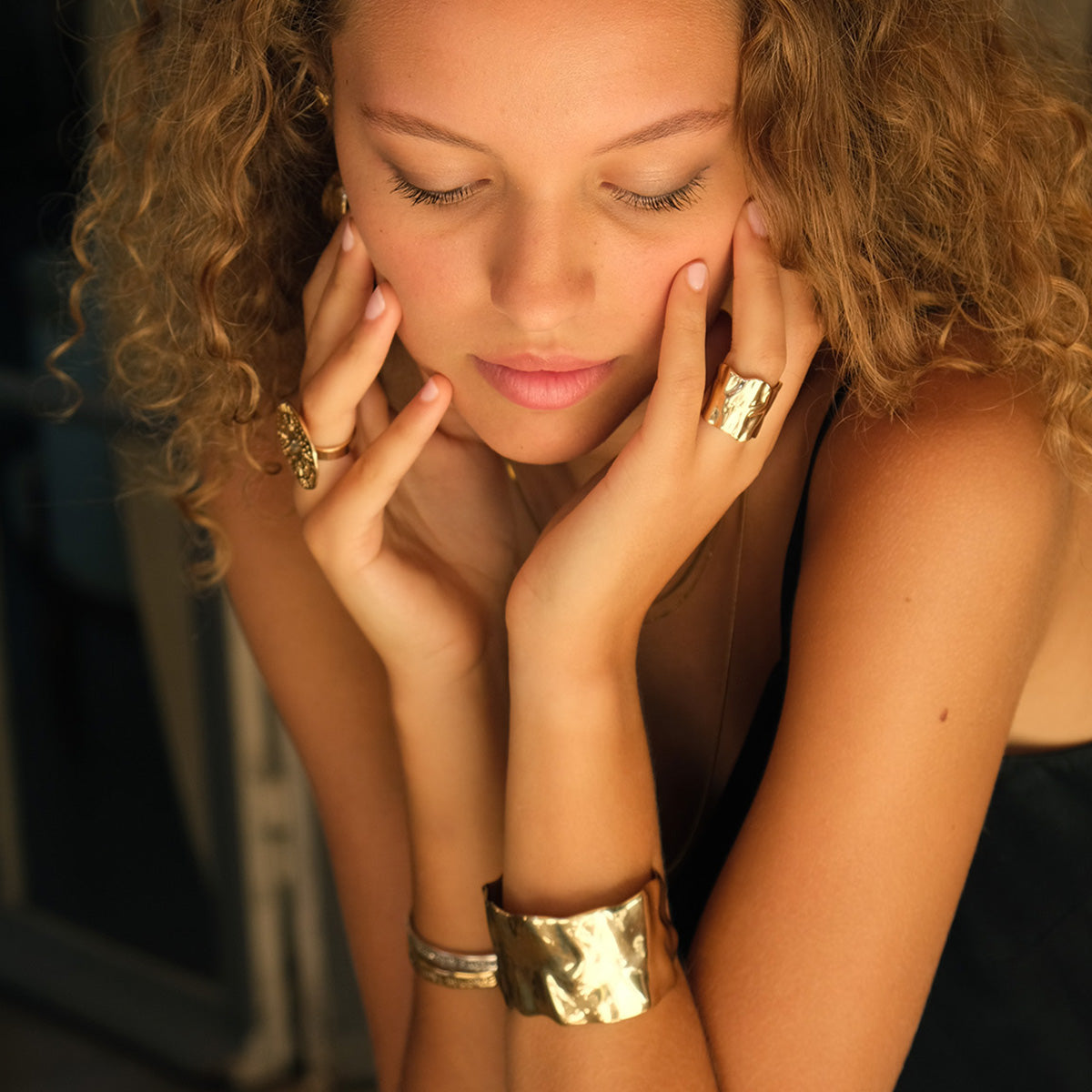 Woman with gold jewelry on her  hands and wrist against a blurred background