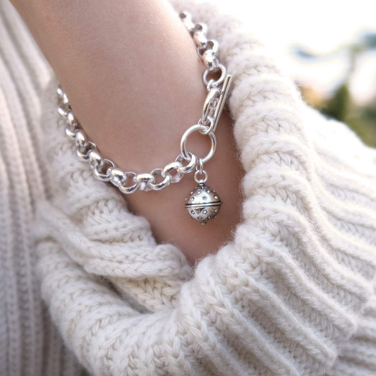 Silver bracelet with a charm on a person wearing a white knit sweater.