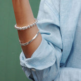 Close-up of a person's arm wearing two silver bracelets with a blurred green background