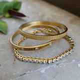 Three gold bracelets with crystal accents on a stone surface.