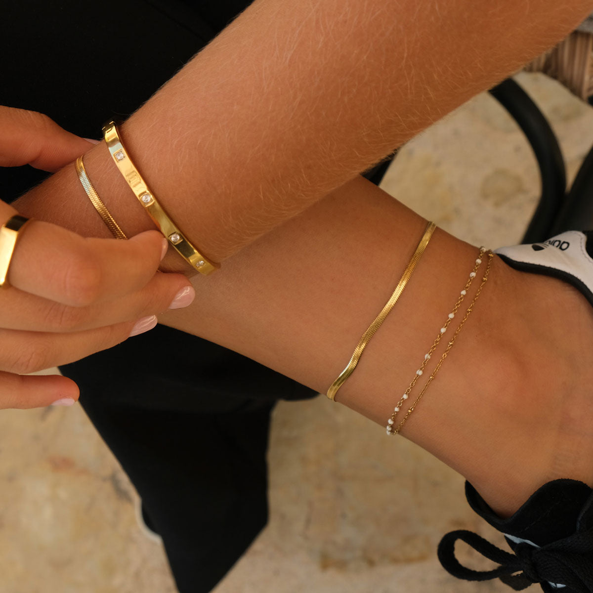 gold bangle with zironia crystals layered with a plain gold bangle and a pearl and gold bracelet