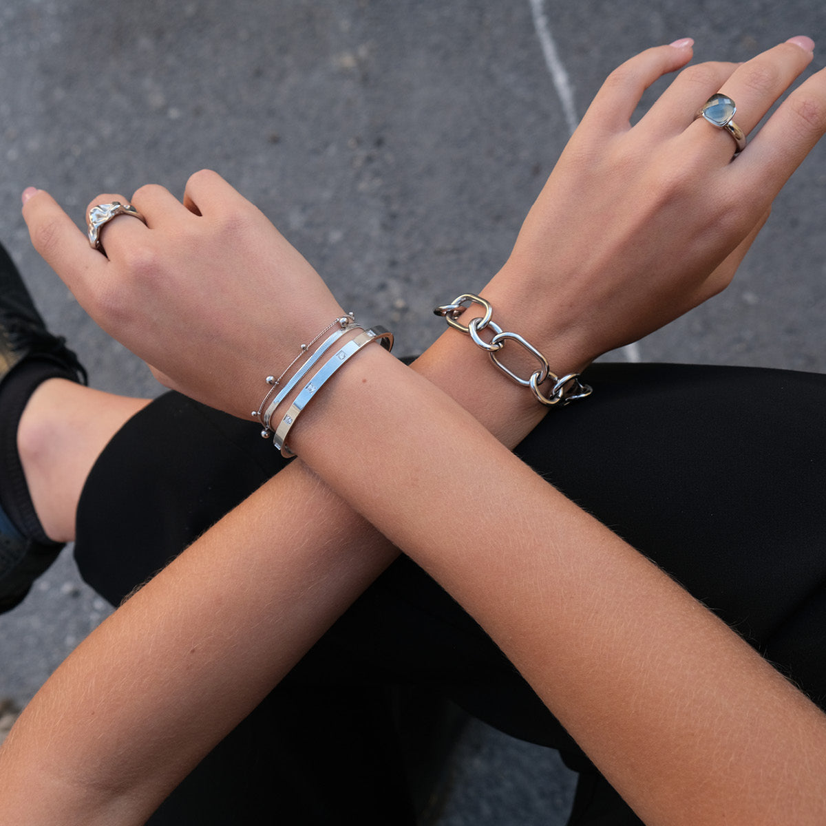 Close-up of a person's arms with multiple bracelets and rings on a blurred background