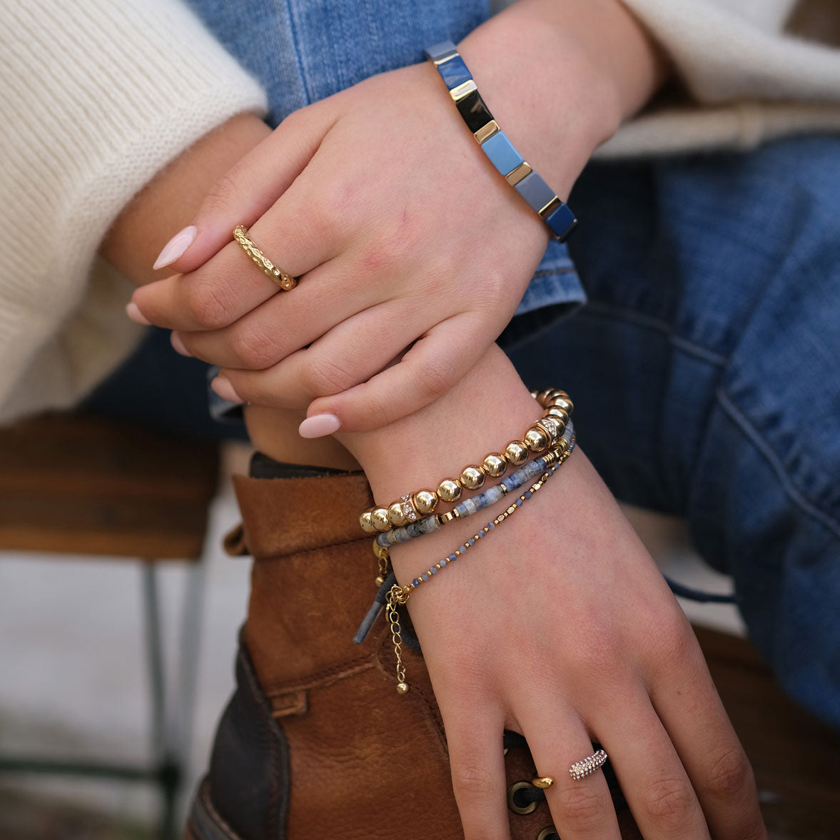 Close-up of hands wearing multiple bracelets and rings with a blurred background