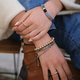 Close-up of hands wearing multiple bracelets and rings with a blurred background