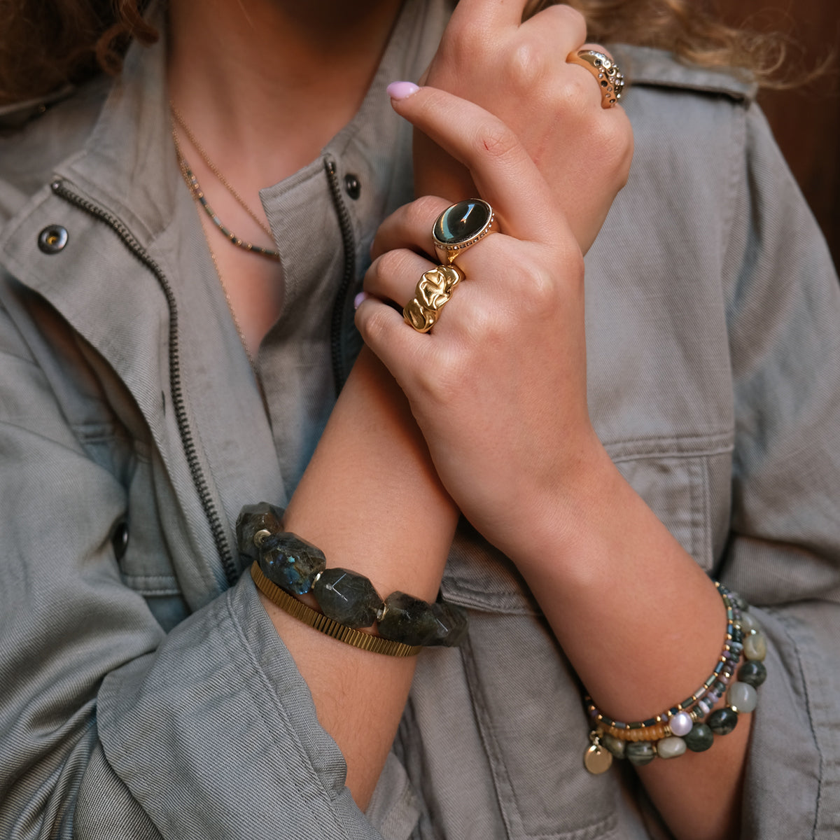 Close-up of a person wearing multiple rings and bracelets on a neutral background