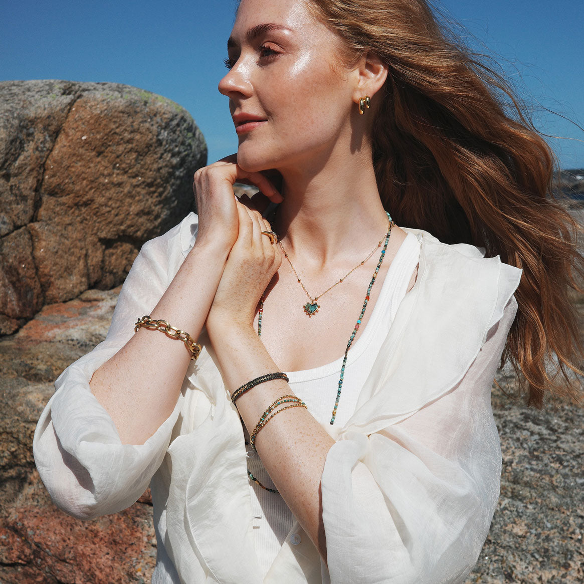 Model wearing a collection of necklaces, earrings and bracelets from A&C Oslo Jewellery. Featuring the heart shaped pendant necklace with gold  beads on the chain.  The heart is made from African Turquoise and the steel chain plated in 14K gold at Cerise NZ.