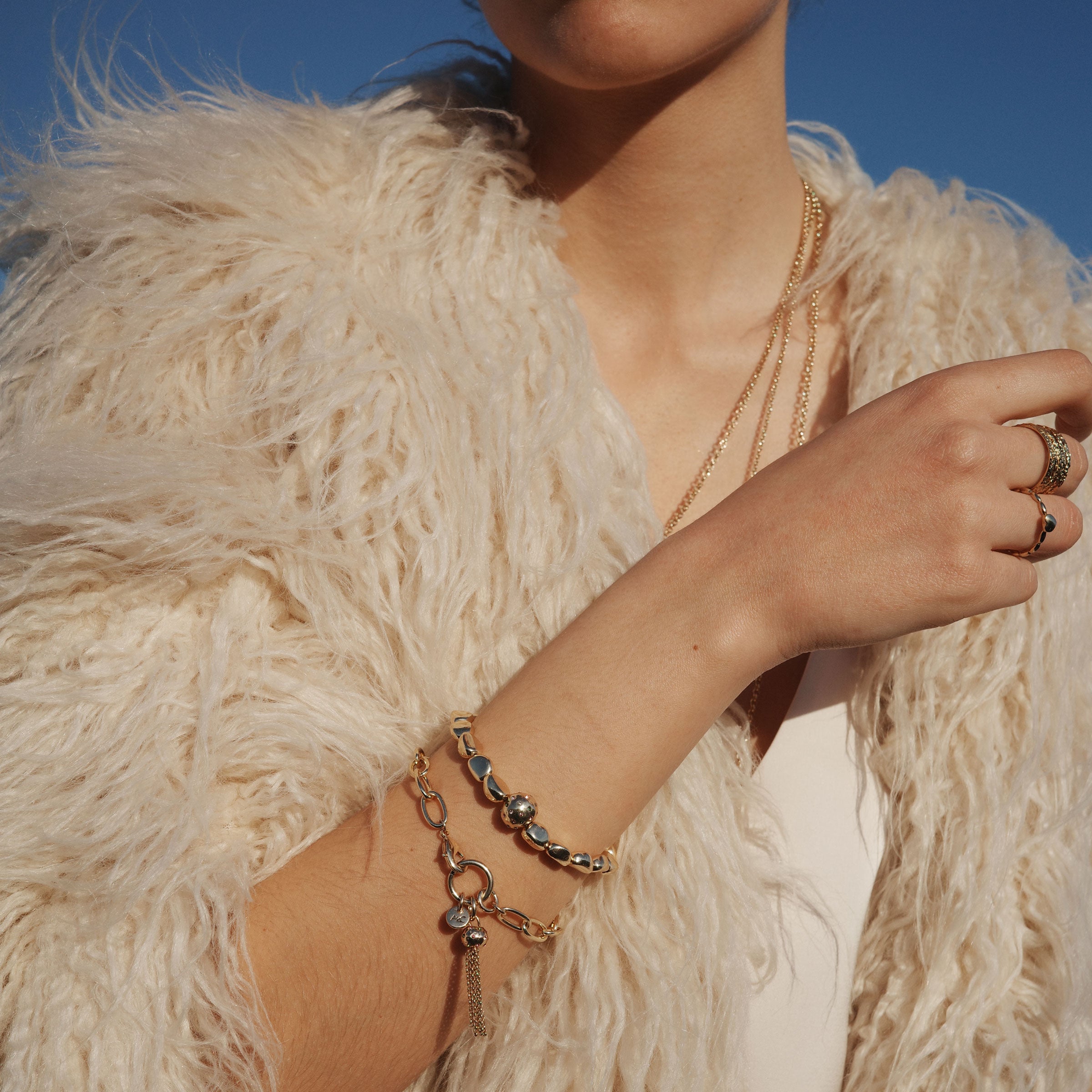 New at Cerise this season  the A&C Oslo Shimmer Collection features this gorgeous Gold Bracelet with tassels gently falling from a medium link chain.  Pictured here on a model showing how it can be matched with other bangles to create a layered look.
The Shimmer Collection is finished in 14K gold plate for stunning shine and durability.