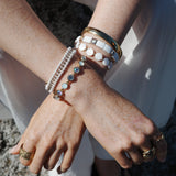 Model wearing A&C Oslo 14K gold plated steel bracelet mixed with other bangle designs including the emamel white tile bracelet and Friendship bracelet in white and gold for a layered look at Cerise NZ