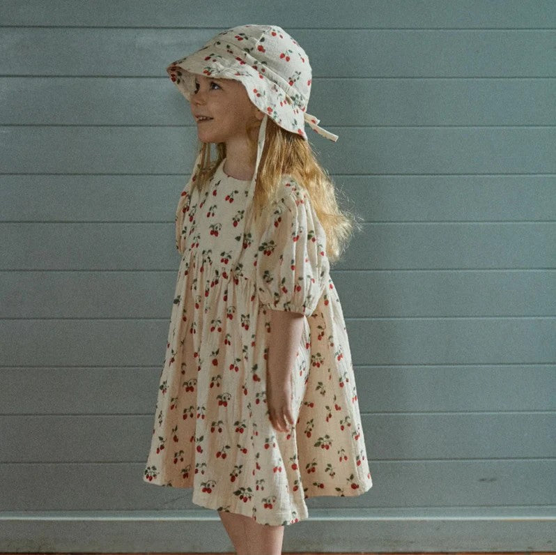 Young girl wearing a natural musline dress with cherry print
