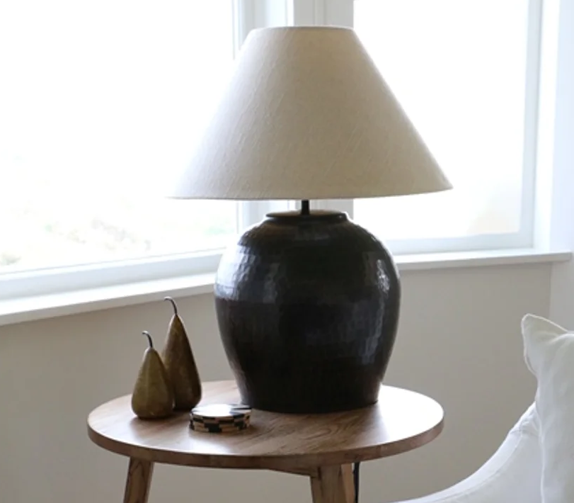 CC Interiors Romo Lampbase shown here with the Biscotti 51cm lamp shade at Cerise. The shade is sold seperately. Handmade from hand beaten aluminium and finished in an antique bronze colour. Shown here on a light wood side  table.