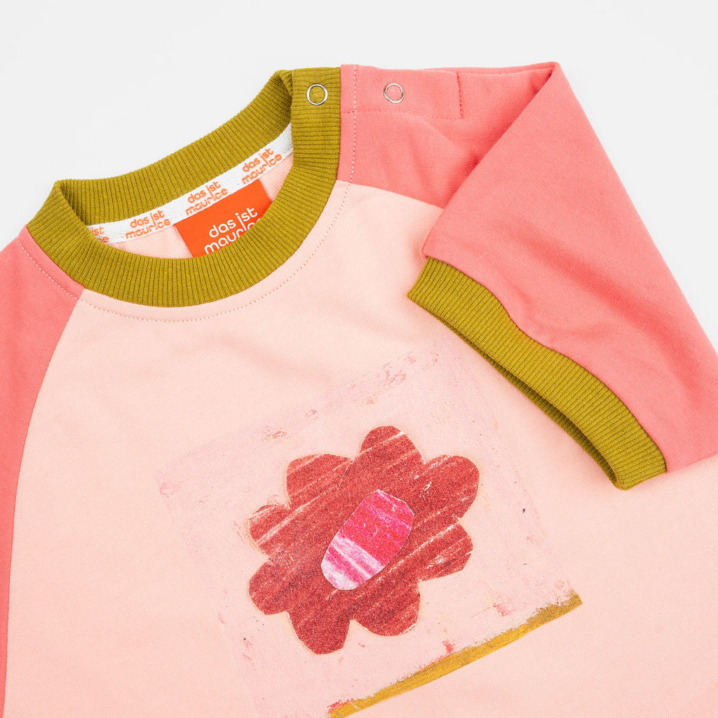 Das Ist Maurice Romper in Pink Petal at Cerise. A sweet, hand-drawn “Pink Petal” artwork sits across the chest, adding a unique and playful touch. Contrasting bright coral raglan sleeves bring a vibrant pop of colour, while olive green ribbed trims.