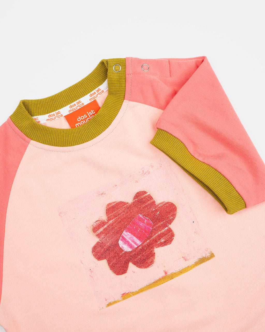 Das Ist Maurice Romper in Pink Petal at Cerise. A sweet, hand-drawn “Pink Petal” artwork sits across the chest, adding a unique and playful touch. Contrasting bright coral raglan sleeves bring a vibrant pop of colour, while olive green ribbed trims.
