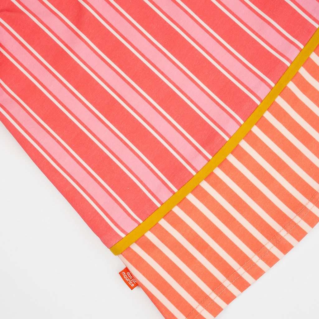 Das Ist Maruice Sleeveless Dress in Coral at Cerise. The relaxed A-line silhouette provides plenty of room for movement, making this sleeveless kids’ dress ideal for active days. Featuring bold coral and peach stripes, the dress has a fun retro-inspired look with a vibrant mustard yellow neckline and contrasting trim