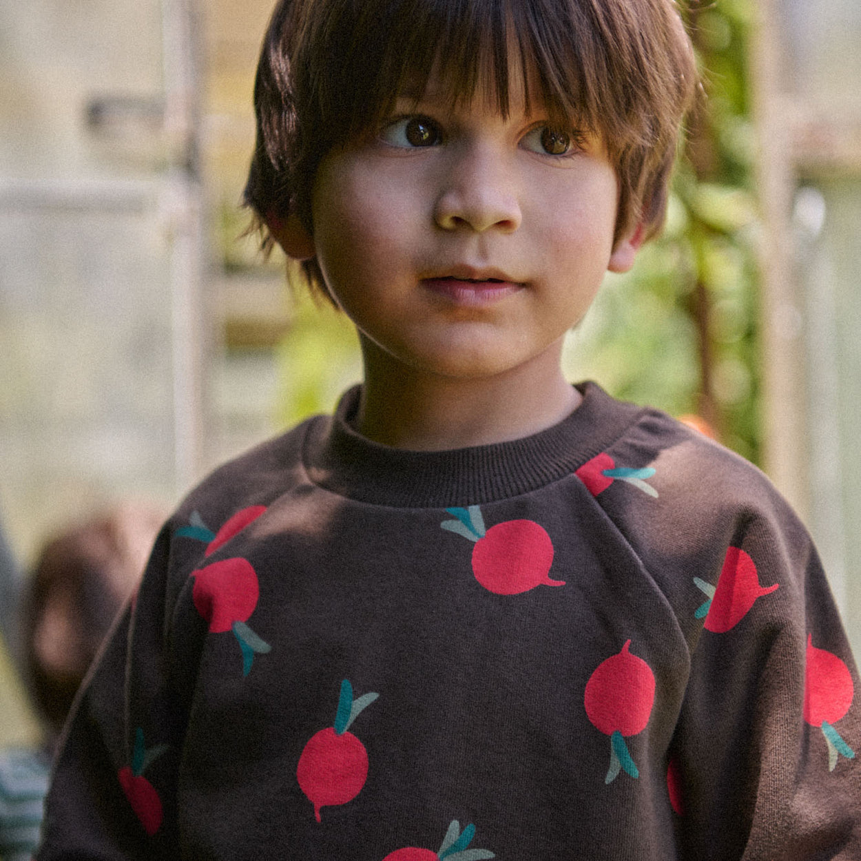Nature Baby Emerson Sweater in Brown cotton knit with radish print in red and green. Has ribbed crew neck and cuffs at Cerise