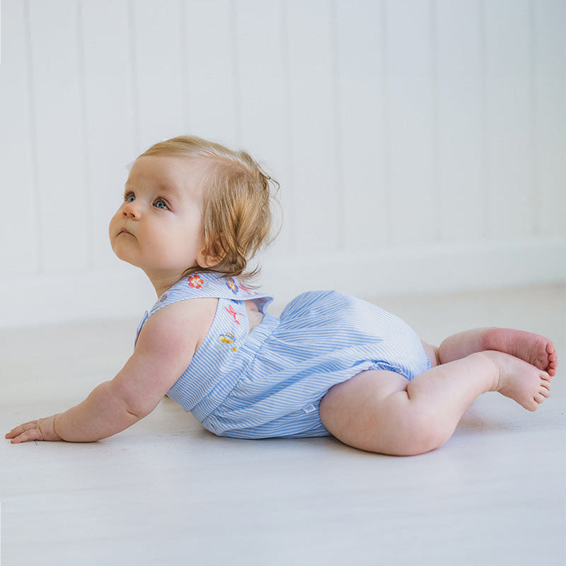 Baby wearing a blue striped romper sitting on a white surface.