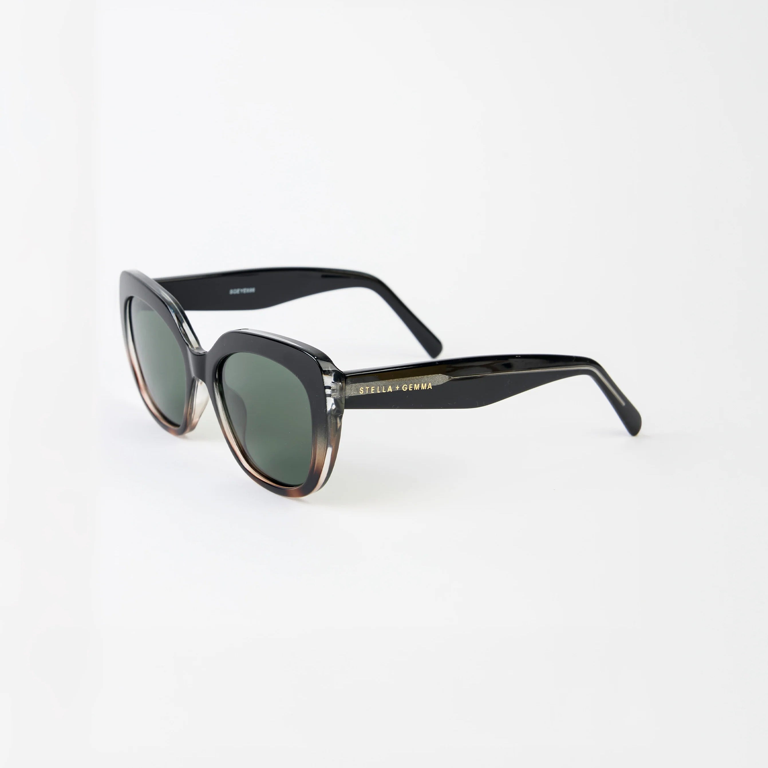 Sunglasses with a transparent tort frame and stella and gemnma branding on arm