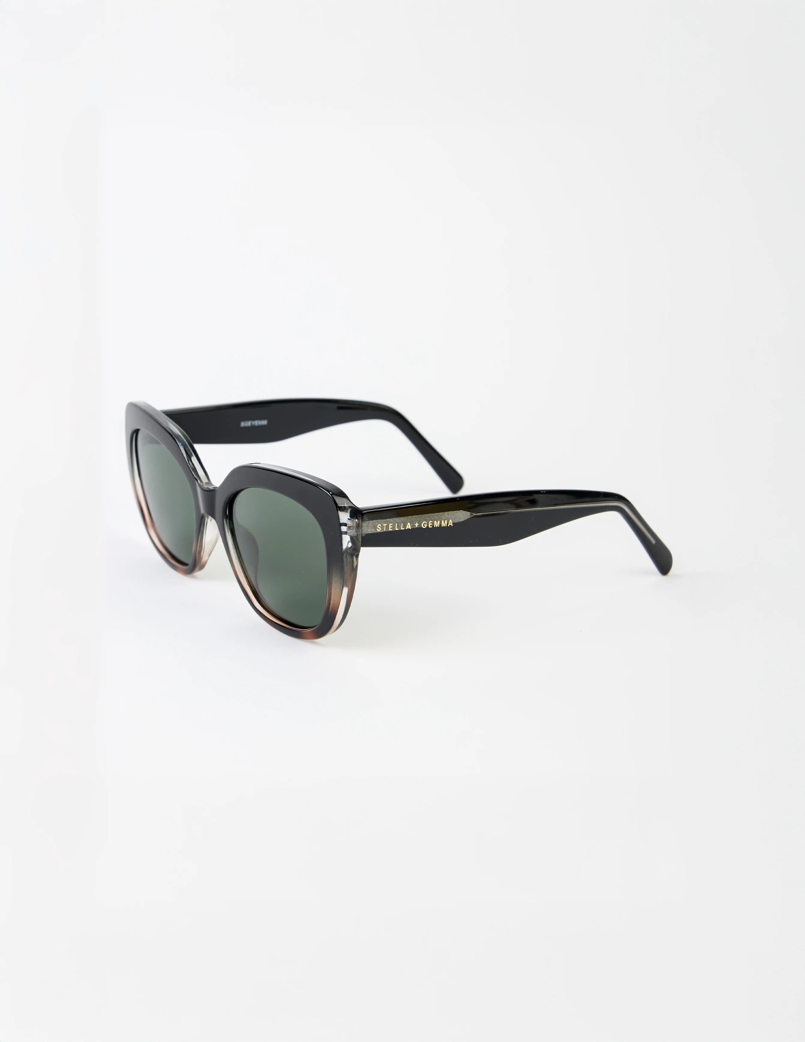 Sunglasses with a transparent tort frame and stella and gemnma branding on arm