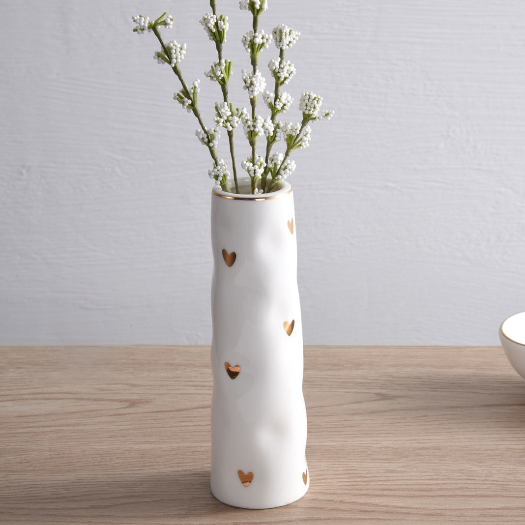White ceramic vase with small gold hearts and gold rim and flowers in it.