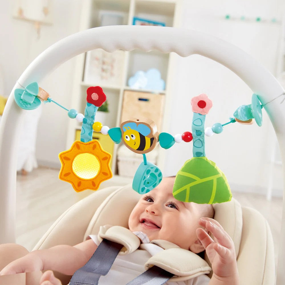 Hape Bumblebee Pram Chain for babies bassinet or pram.  Suitable for ages 0-5 months and features a hanging wooden bee, a textile sunflower, a leaf with a bell inside, wooden triangles, flowers, and colorful beads at Cerise