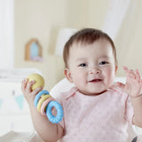 Baby holding The Hape Rattling Rings Teether at Cerise.  Its made from safe, rice-based materials. This smiling baby teething toy includes three colourful rattling rings that encourage sensory exploration, along with a teether ring to help comfort sore gums during teething.
