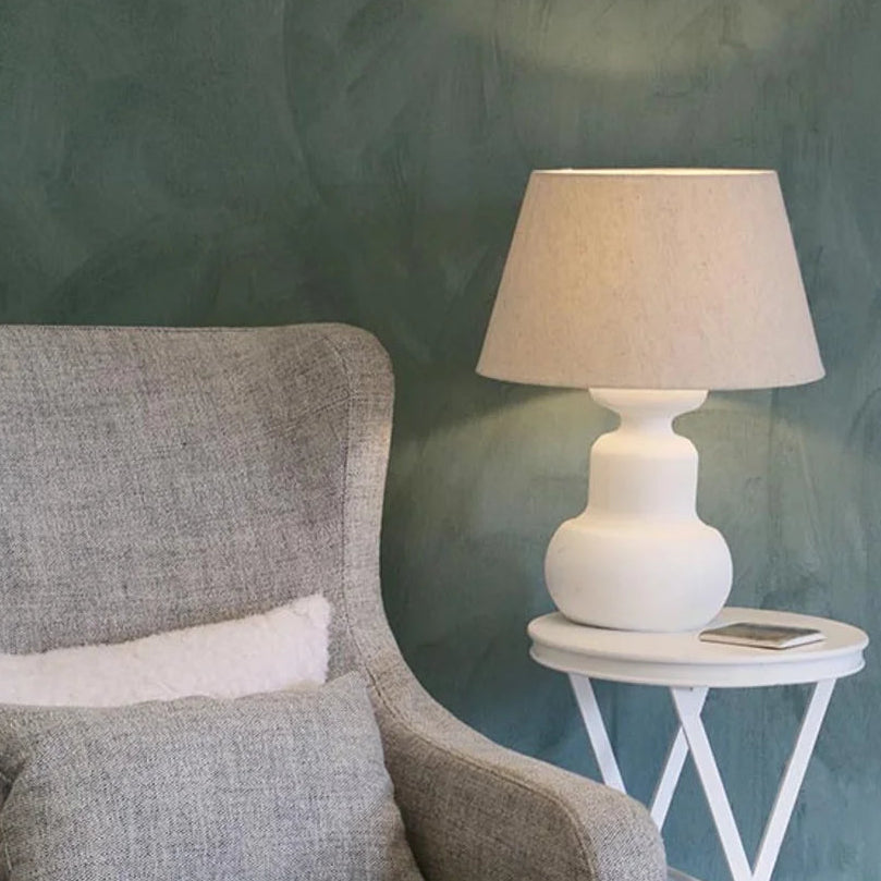 White wooden urn lamp base shown with oatmeal coloured drum shade on white side table at Cerise