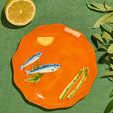 La La Land Stoneware Plate at Cerise featuring an embosed design with sardines, asparagus and Lemons on an orange background.