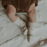 Baby wearing Lamington Newborn naturals merino socks in  Fox design at Cerise. Feature grey crosses on a white backround