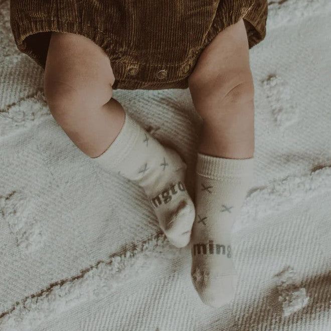 Baby wearing Lamington Newborn naturals merino socks in  Fox design at Cerise. Feature grey crosses on a white backround