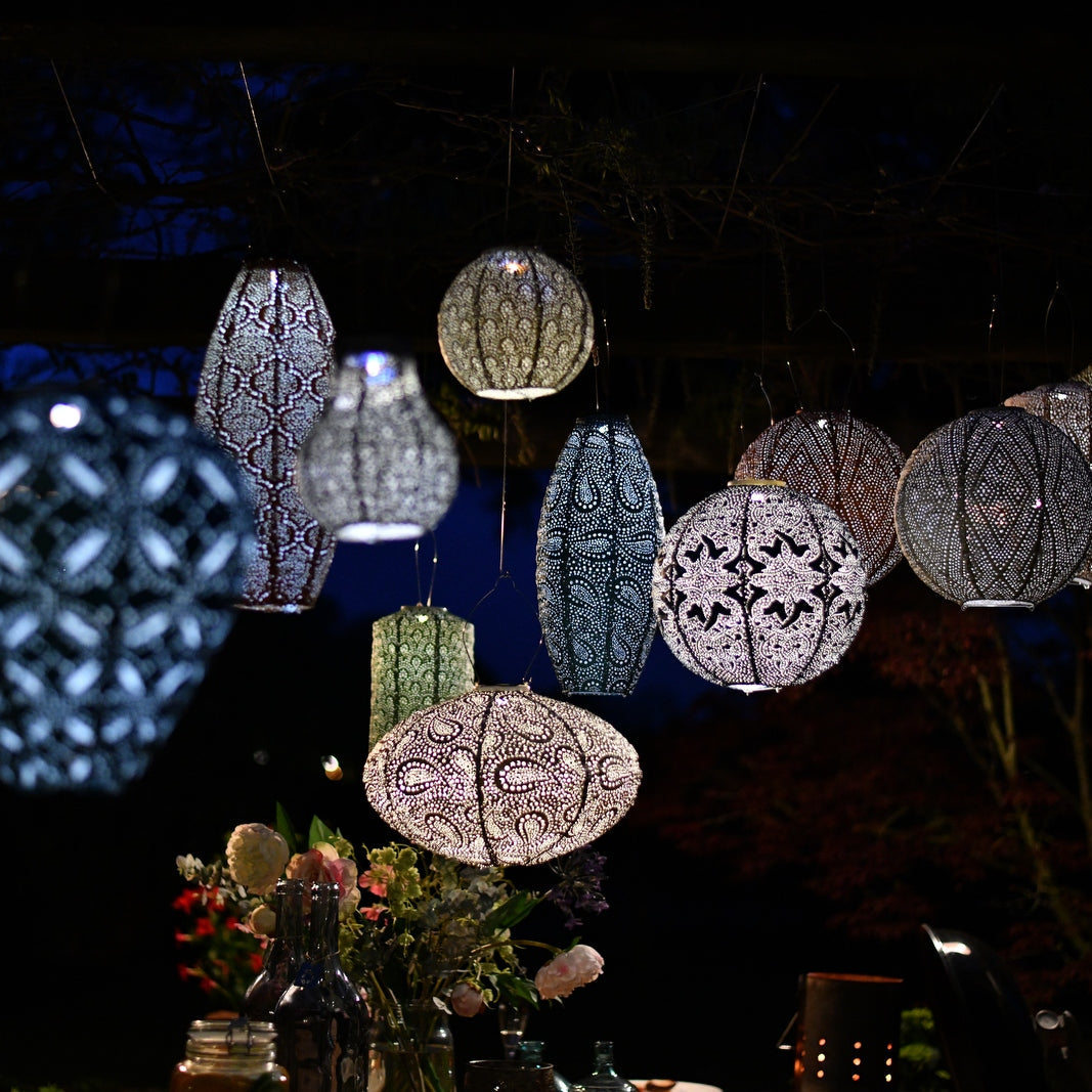 Group concept photo of hanging lumiz solar lanterns at dusk. Showing intricate design patterns and colours as they glow in the evening.