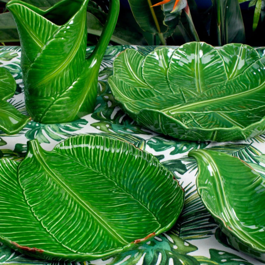 Green leaf-patterned ceramic items on a tablecloth with a similar leaf design.