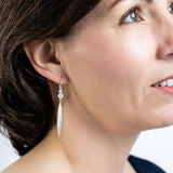 Model wearing silver  fish hook icon earrings with a flax leaf drop.