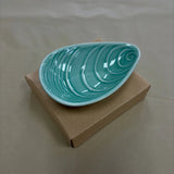 Aqua mussel shaped bowl on cardboard box.