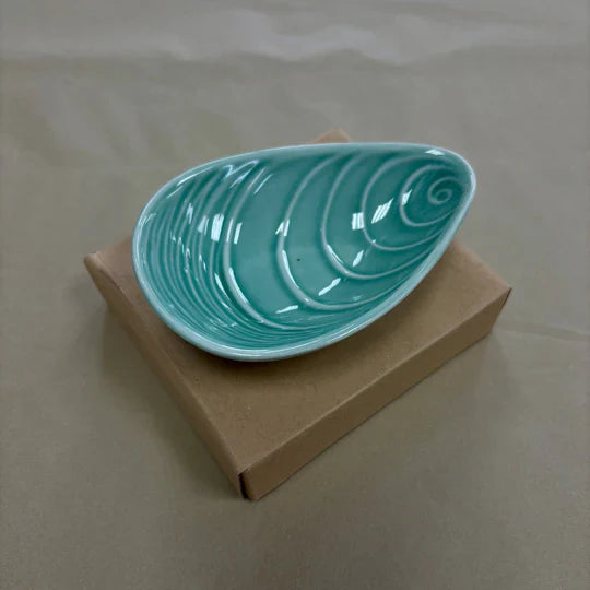 Aqua mussel shaped bowl on cardboard box.