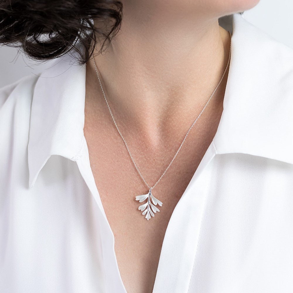 Model wearing a silver necklace with a  NZ hen and chicken fern pendant