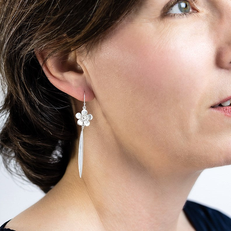 Model wearing Sterling 
silver NZ Manuka flower earrings with a harakeke flax leaf drop