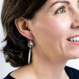 Model wearing Sterling silver NZ Manuka flower earrings in a circle with a flax leaf drop.