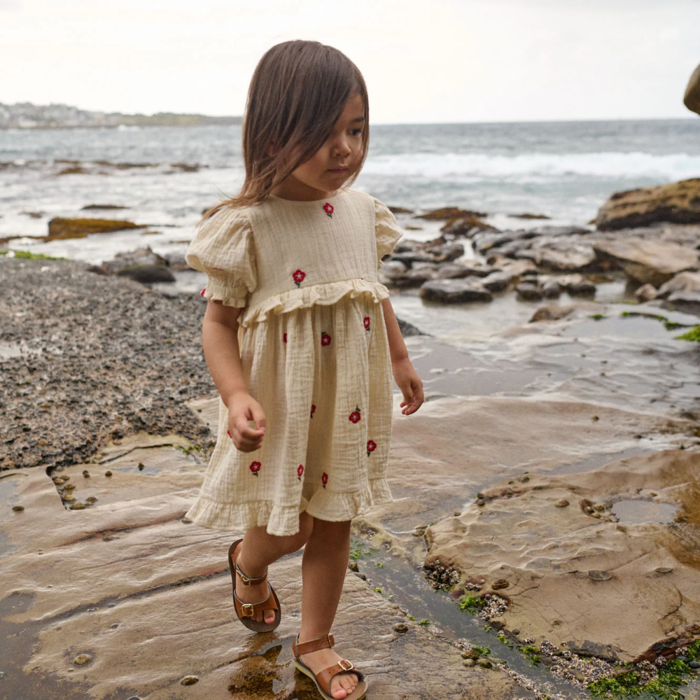 Nature Baby Valentina Dress in Red Flora at Cerise.  Made of muslin and features red embroidered flowers on a natural background.  Stunning puffed sleeves and frill at the waist and hemline.