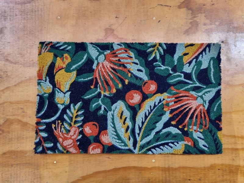 Decorative doormat in a pohutakawa and kowhai design in dark blue, teal , green, red and yellow tones