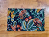 Decorative doormat in a pohutakawa and kowhai design in dark blue, teal , green, red and yellow tones