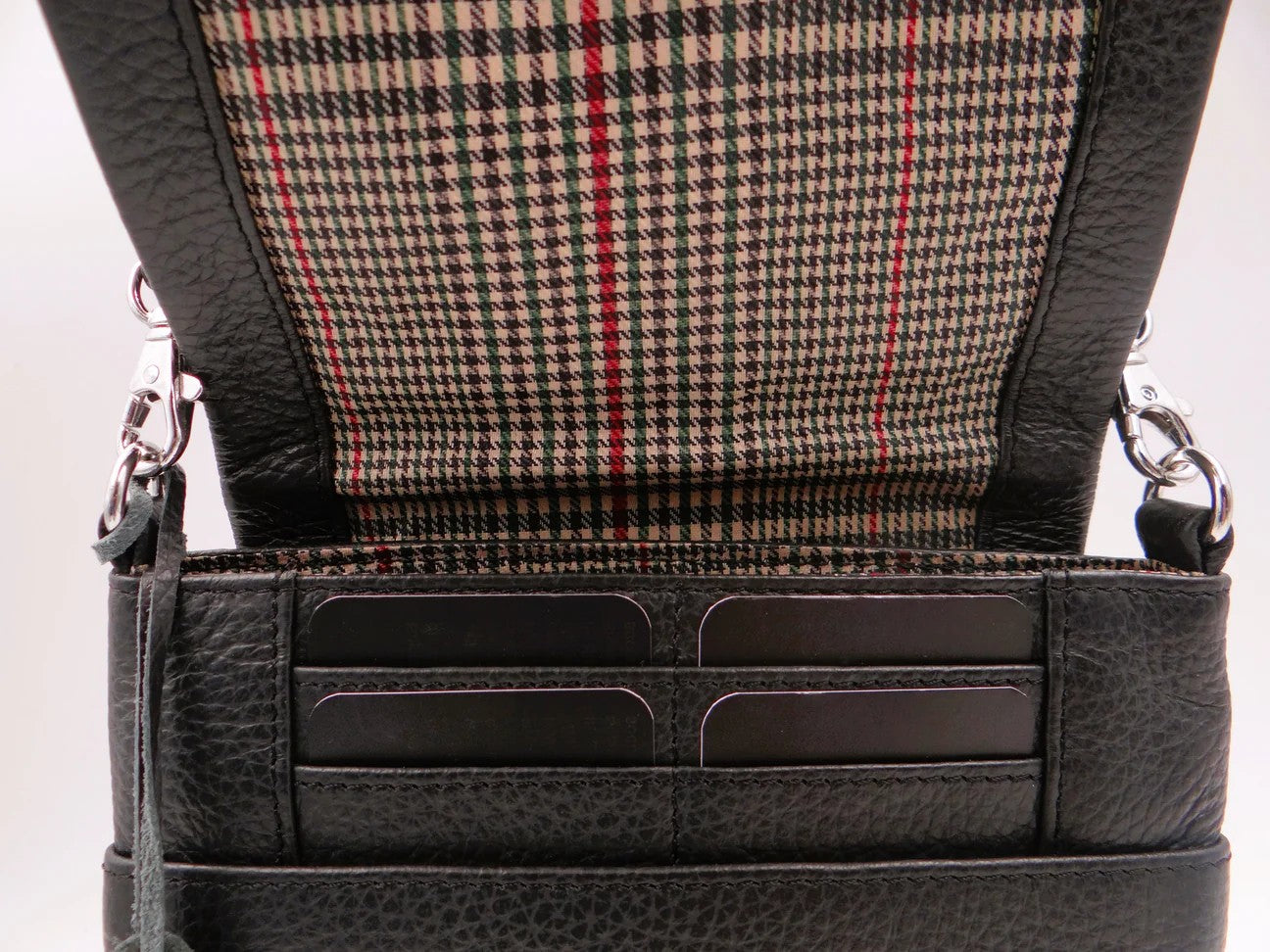 Close-up of a black leather bag showing card slots with plaid interior lining.
