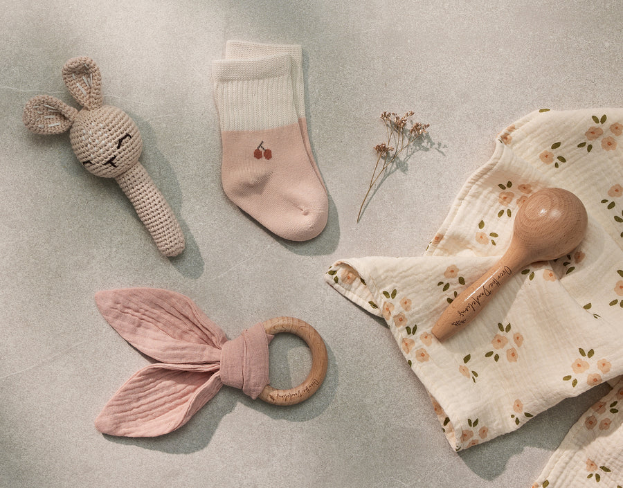 Over the Dandelions Set of 2 Baby Socks in soft pink and ivory with a cherry motif  design at Cerise. Made from soft organic cotton to fit newborn babies size 0 to 6 months. Shown here with Bunny Crochet Rattle and Daisy Bup cloths as a newborn baby gift idea.