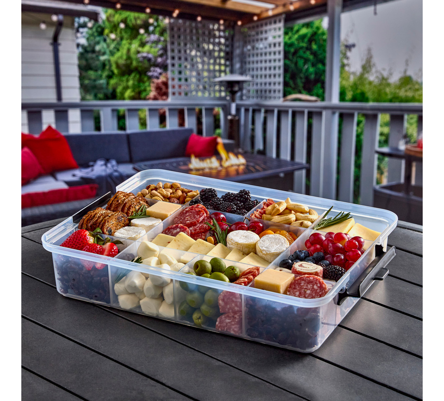 Transparent food storage container with assorted snacks on a wooden deck