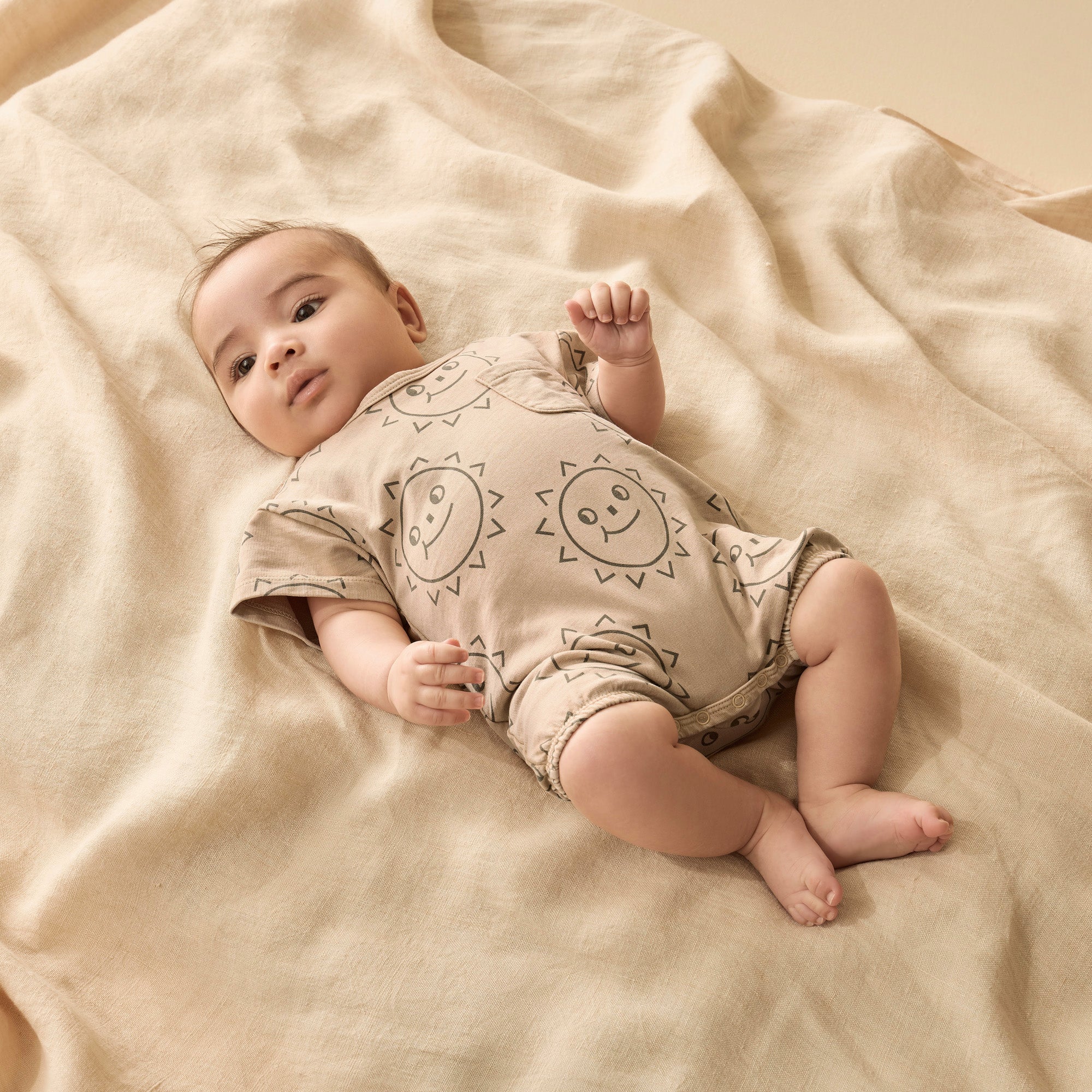 Baby wearing grow suit in caramel colour with brown sun faces. dome crotch and short sleeves with front feature pocket