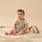 Baby wearing Caramel base with brown sun faces baby overall with tie straps, front pocket and crotch dome opening.  Short legs