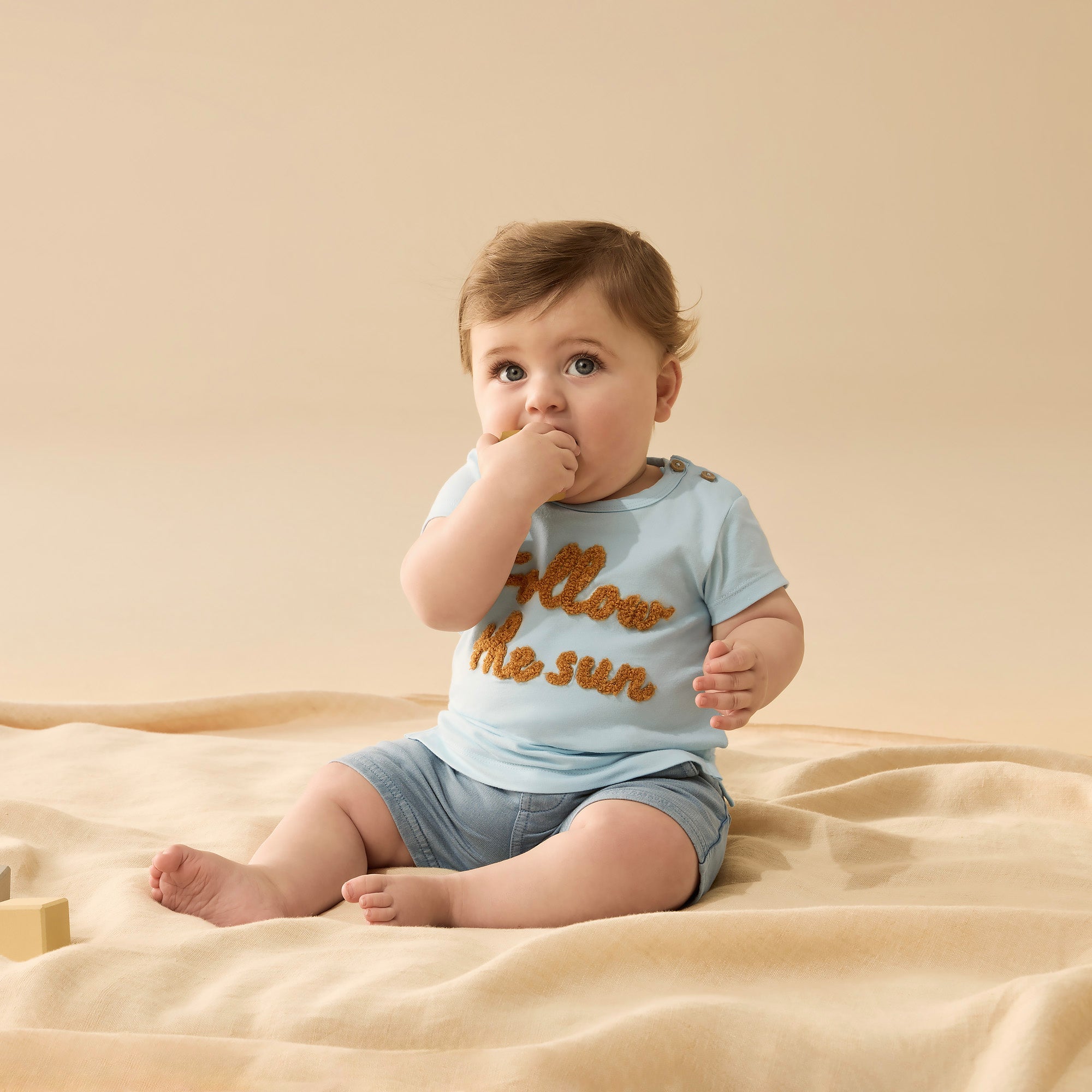 Baby wearing light blue tee shirt with follow the sun embroidered logo on front