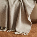 The Magnus Throw in Quartz colour at Cerise.  Made from 100% New Zealand wool, this large blanket which measures 150 x 183cm is  cosy and comfortable.  Featuring a classic herringbone weave with contrast fringe, in a natural quartz colour.