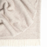 The Magnus Throw in Quartz colour at Cerise.  Made from 100% New Zealand wool, this large blanket which measures 150 x 183cm is  cosy and comfortable.  Featuring a classic herringbone weave with contrast fringe, in a natural quartz colour.