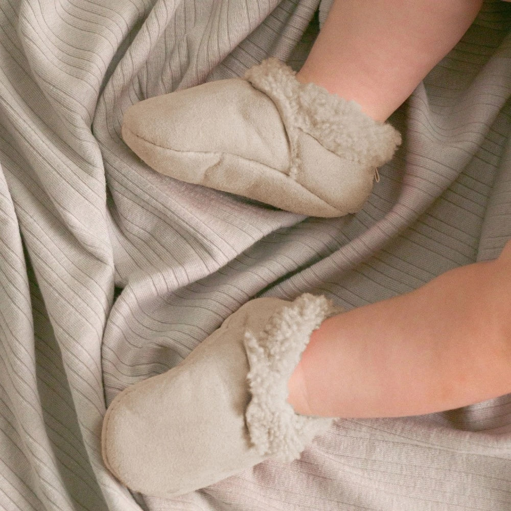 Concept photo of baby wearing Woolbabe Lambskin Booties for baby in a soft natural Toetoe colourway at Cerise. Made in New Zealand.