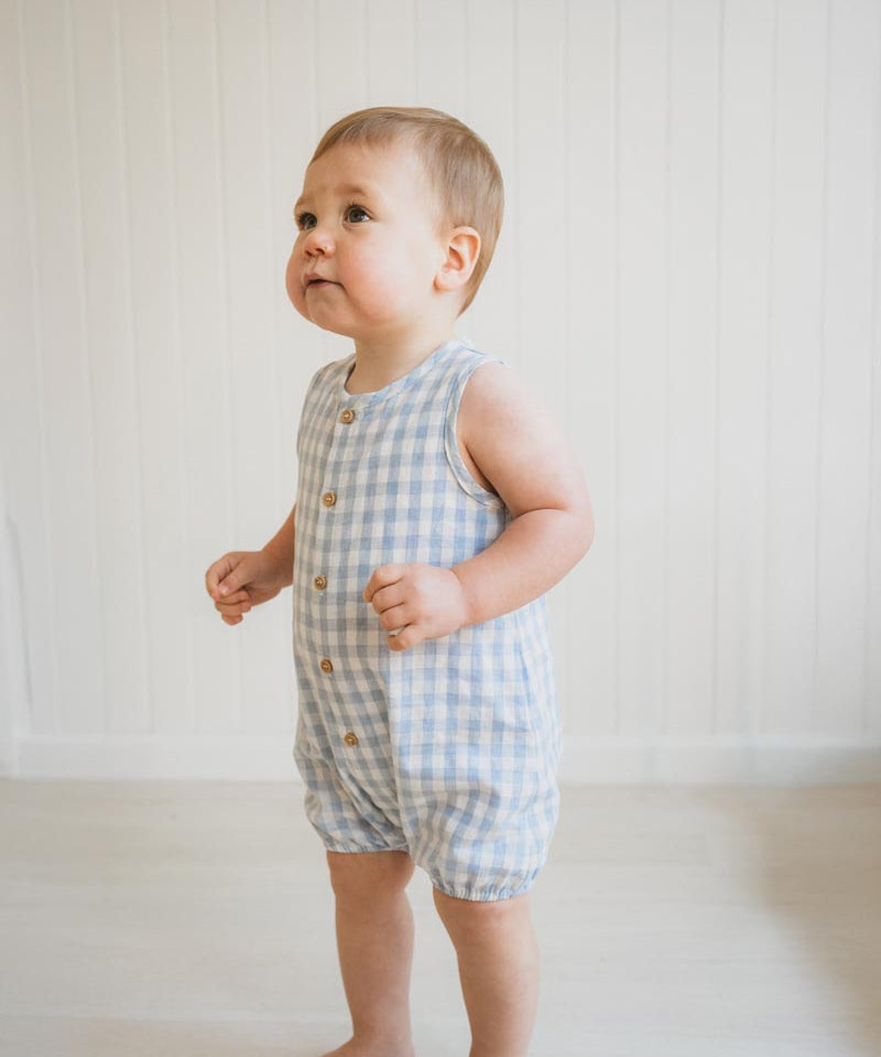 Baby wearing a blue checkered romper against a white background