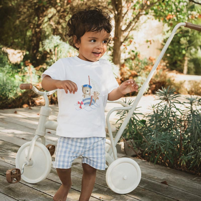 Child standing next to a white tricycle in a garden setting